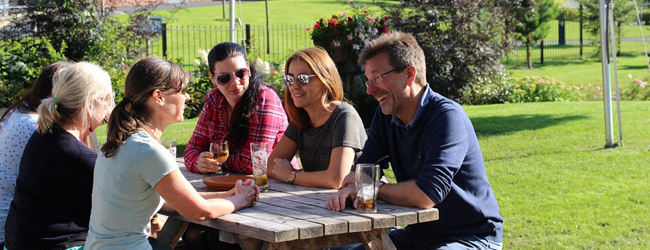 Ein Gruppe Erwachsener sitzt draussen an einem Tisch und spricht miteinander