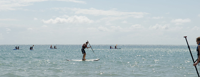 Stand-up-Paddeling bei einer LISA! Schülersprachreise auf Jersey Auf dem glitzernden Meer befinden sich mehrere Schüler, die auf dem Paddelboard stehen oder sitzen